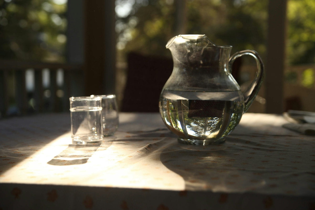 Glaskaraffe mit Wasser und zwei Gläser auf einem Tisch im warmen Sonnenlicht