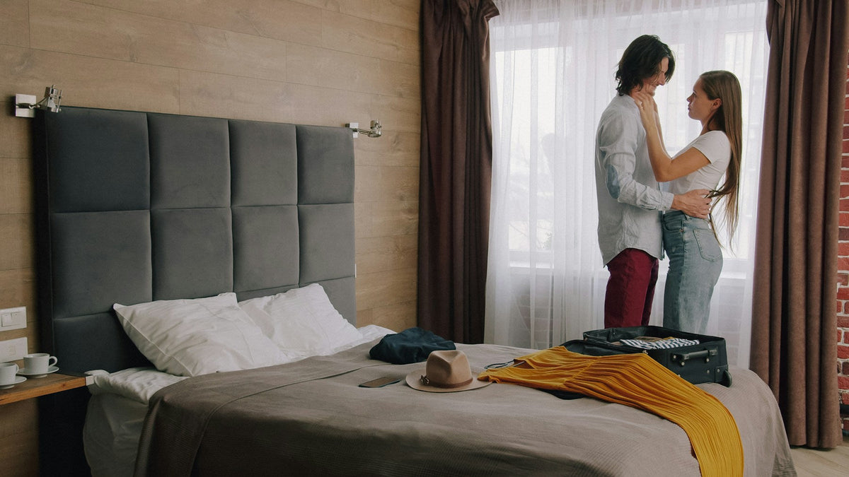 Verliebtes Paar umarmt sich im Hotelzimmer, auf dem Bett liegt ein offener Koffer