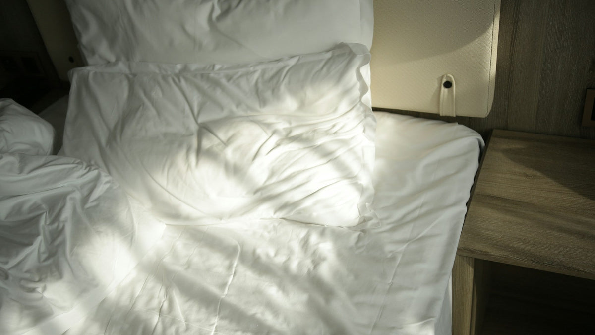 Zerwühltes weißes Bett neben einem Nachttisch im Morgenlicht
